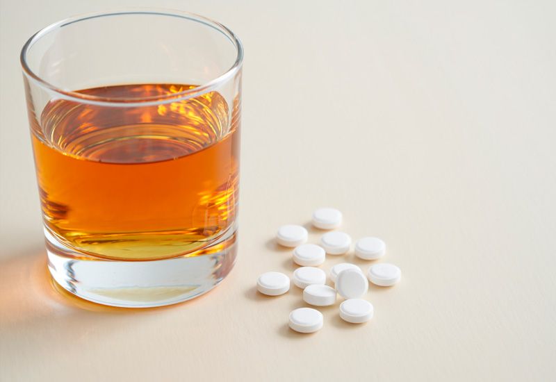 Стакан с янтарным алкоголем и рассыпанные белые таблетки на светлой деревянной поверхности